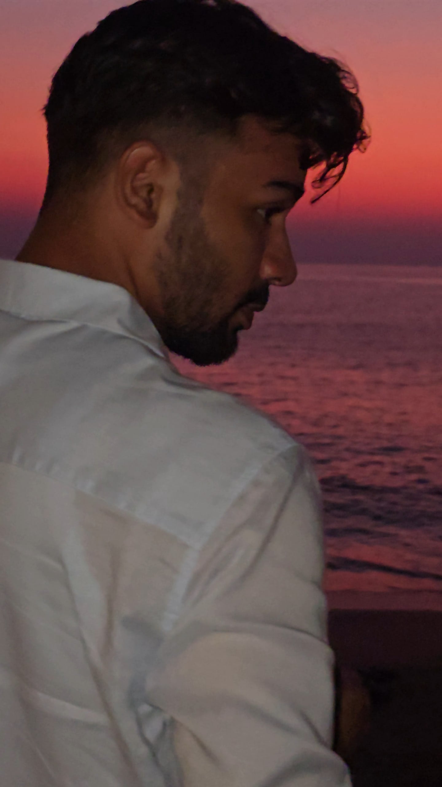 Sunny Prajapati in a white shirt, looking over his shoulder at the sea at dusk